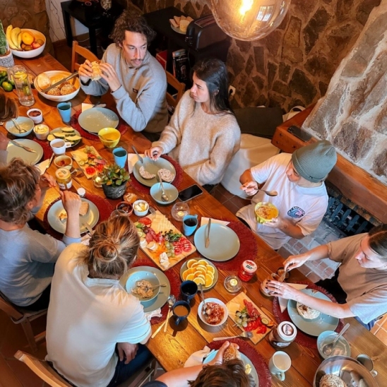 A cozy breakfast scene with friends or family gathered around a table, sharing a meal. Plates filled with delicious food, coffee cups, and smiles create a warm and inviting atmosphere