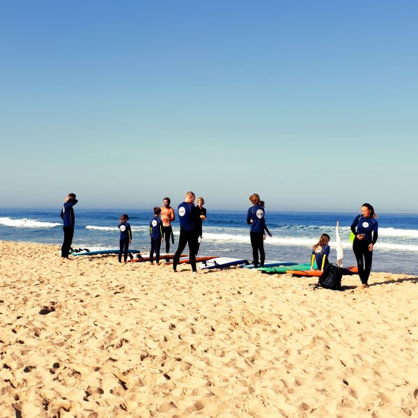 A group of enthusiastic surfers gathers on the sun-kissed beach, attentively listening to their instructor's guidance before hitting the waves. The camaraderie and anticipation among the surfers reflect the excitement of learning and the vibrant surf culture.