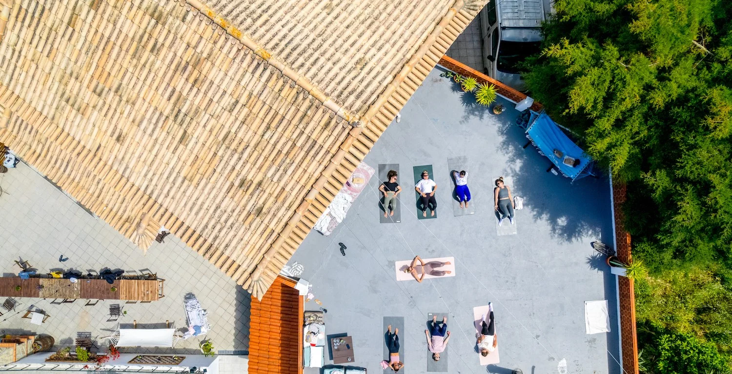 Top-down view of The Far End Surf House property with eight people lying on yoga mats on the sun terrace.