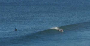 Person paddles into a wave at Praia da Areia Branca beach in Portugal.