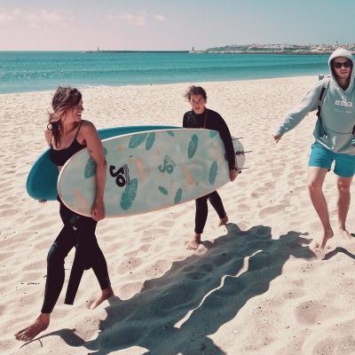 Two girls carrying a surf boards on the beach.